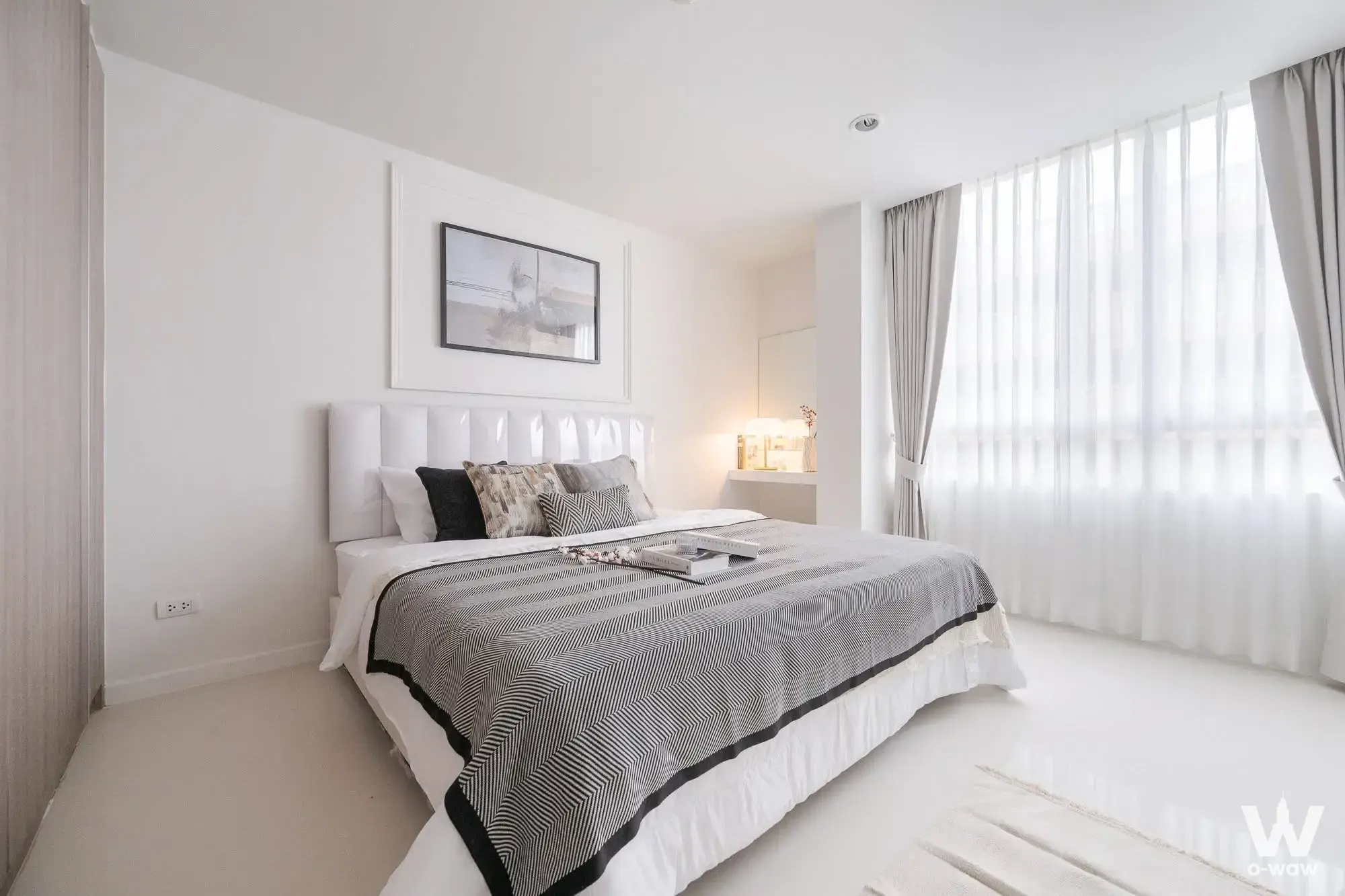 Bright bedroom with white tufted headboard, neutral bedding, and large framed abstract artwork