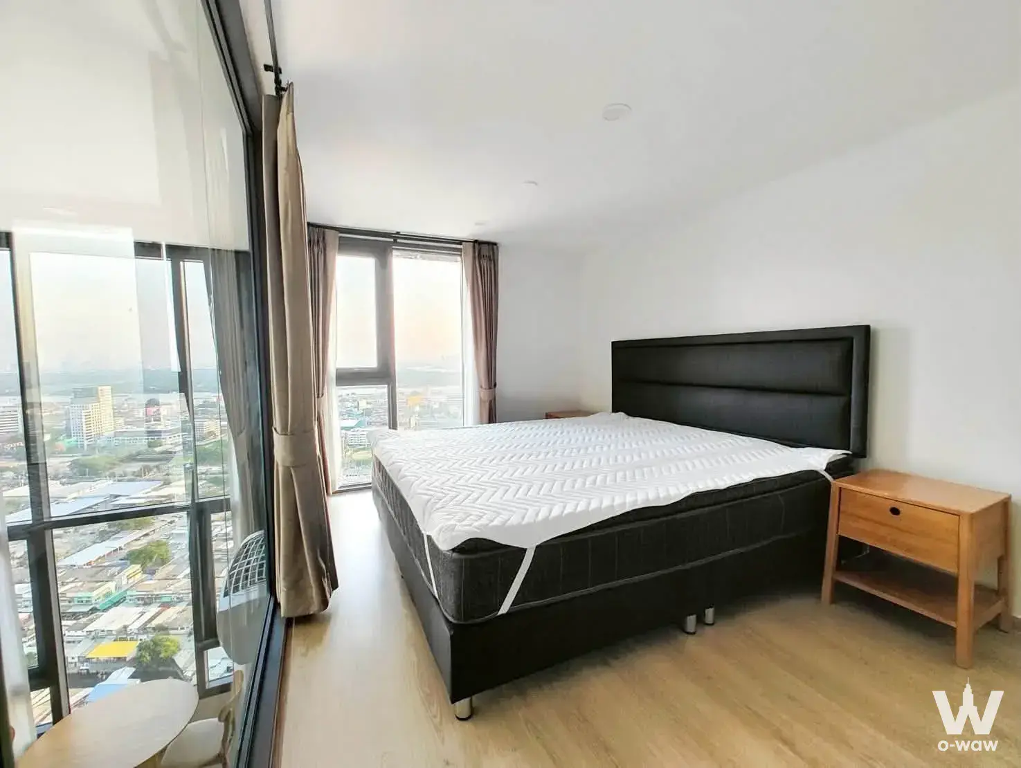Minimalist bedroom with black upholstered bed, floor-to-ceiling windows, and urban skyline view in Life Rama 4 Asoke