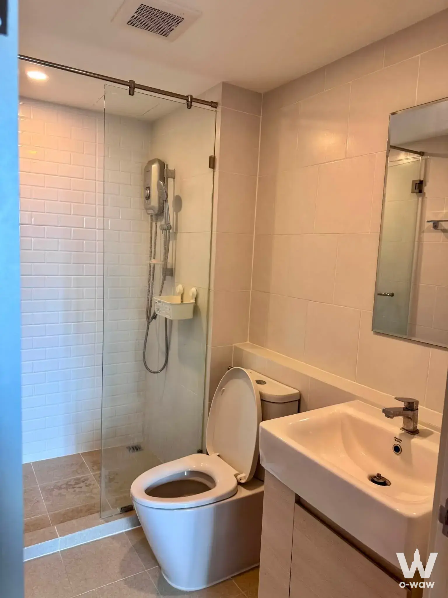 Compact modern bathroom with glass shower, beige tiles, and vanity in Chewathai Hallmark condo