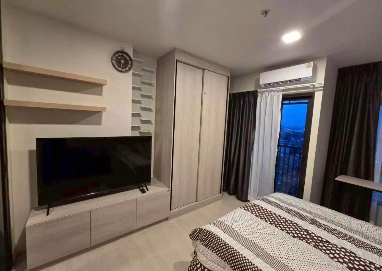 Furnished bedroom with built-in wardrobe and TV unit overlooking city lights in FLO by Sansiri