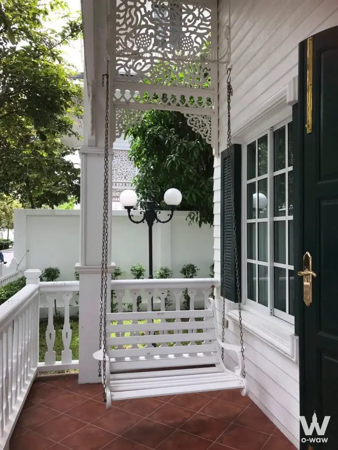 Covered porch of Fantasia Villa2 with white wooden swing bench, lattice ceiling panel, and green-shuttered windows
