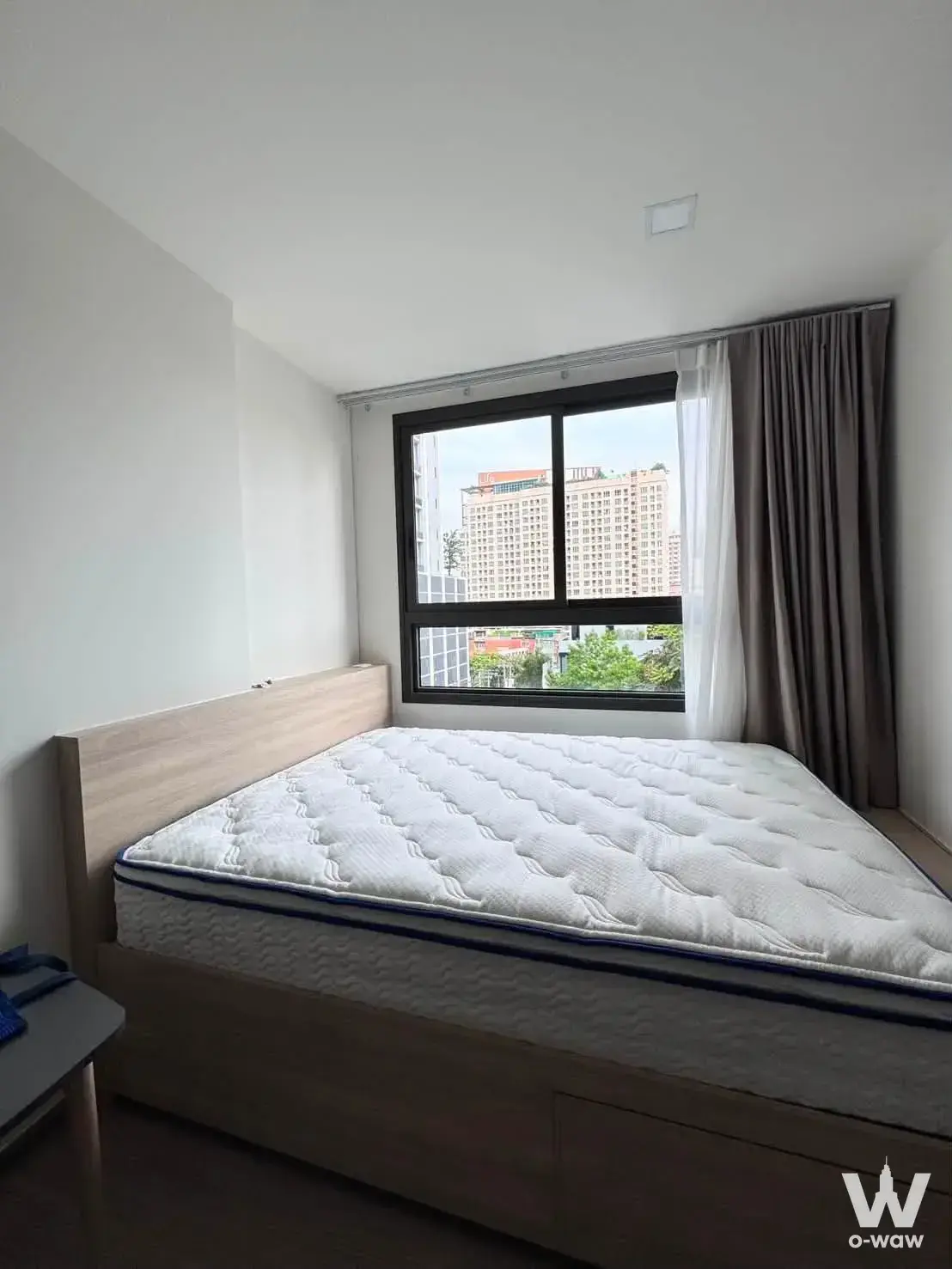Minimalist bedroom in The Muve Pradipat with platform bed and city view through sliding window