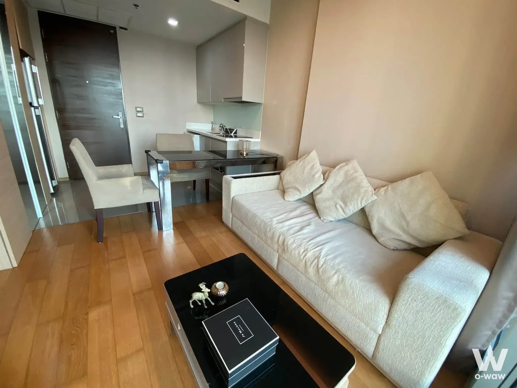 Open-plan studio in The Address Asoke with a beige sofa, dining table, and warm honey wood plank flooring