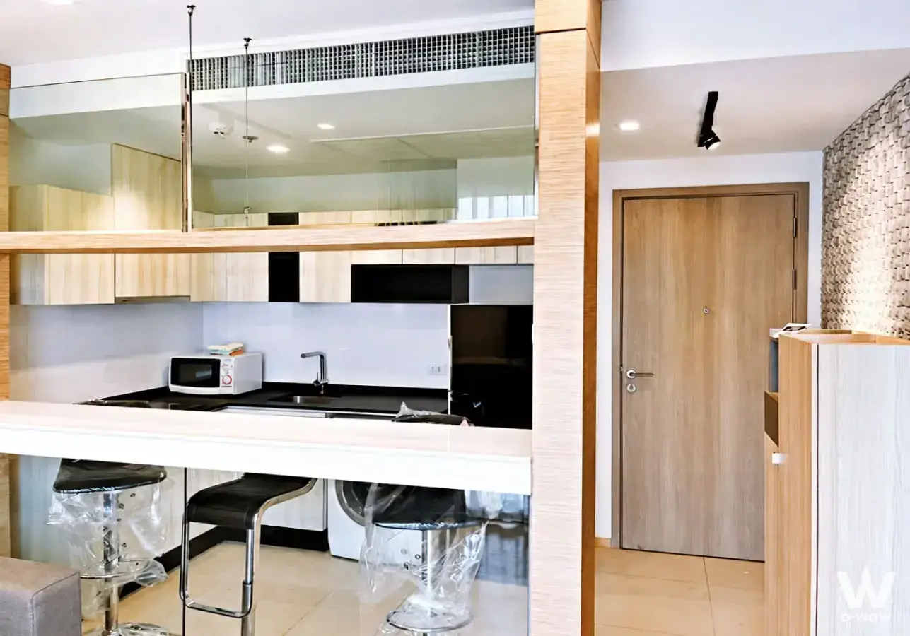Studio kitchenette with light wood cabinets, black glossy base units, and breakfast bar stools