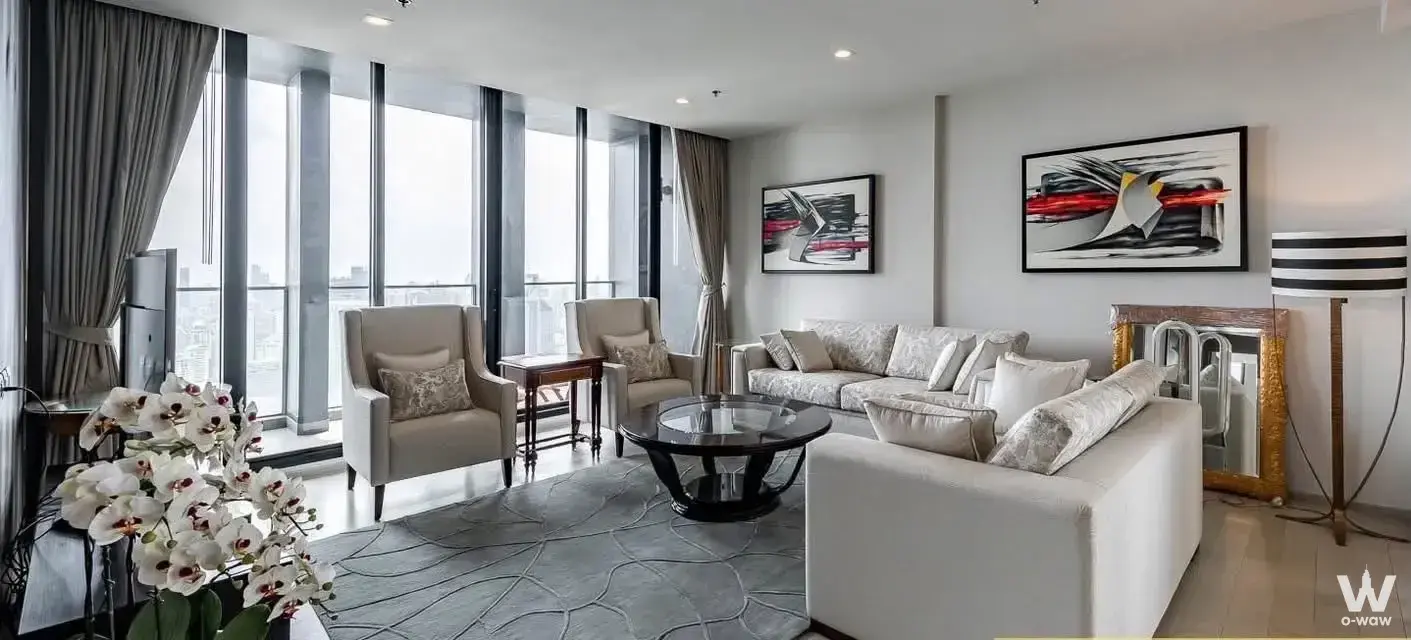 Noble Ploenchit 2-bed condo living room with beige sofa, orchid, and city skyline view
