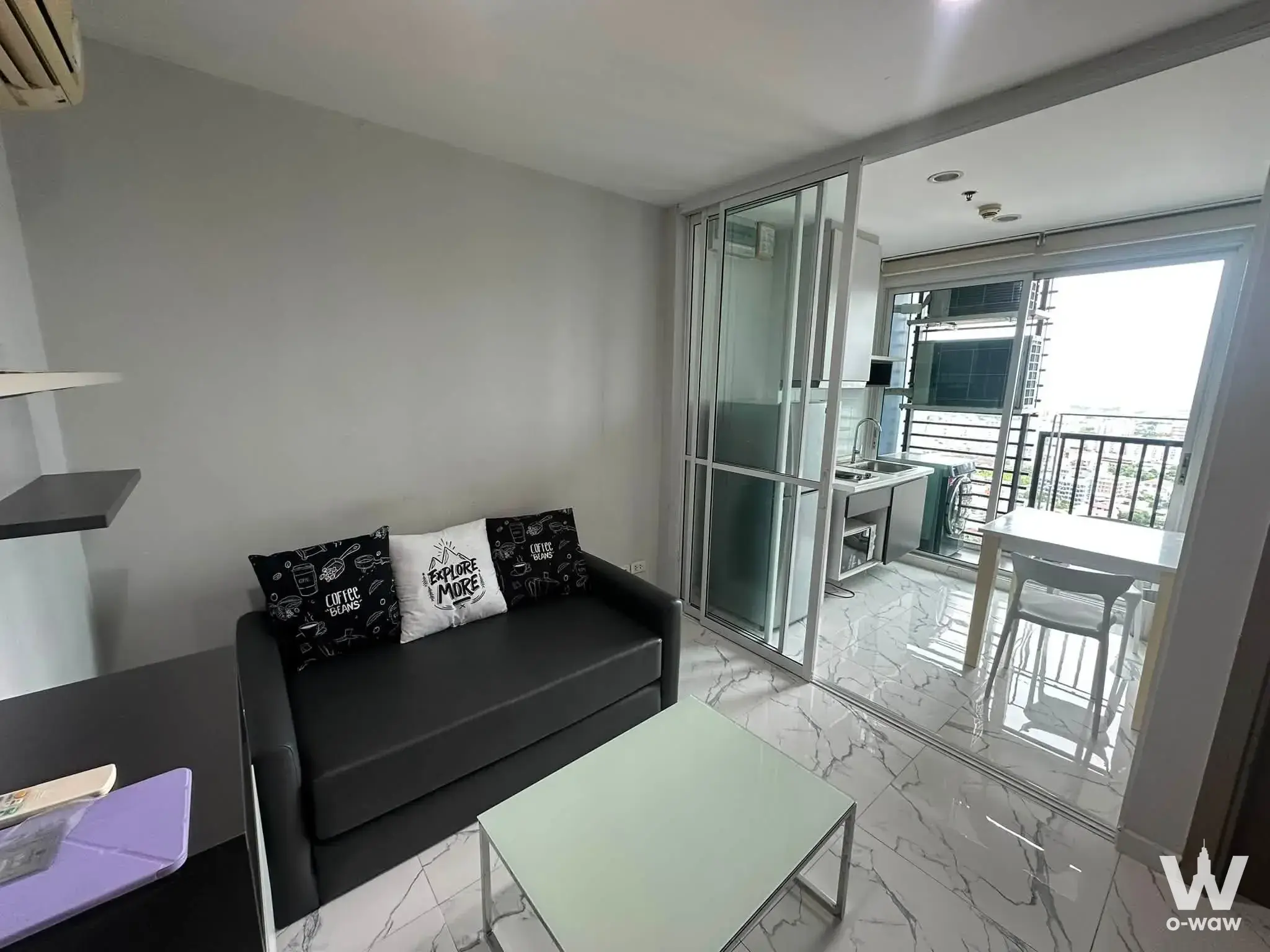Living room in THE BASE Sukhumvit 77 condo featuring glass coffee table and balcony access