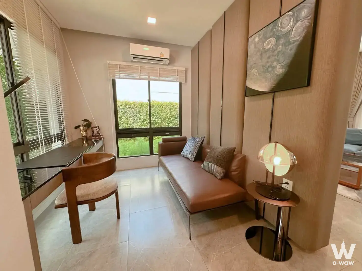 Condo living area with leather daybed, study nook desk, and green hedge view