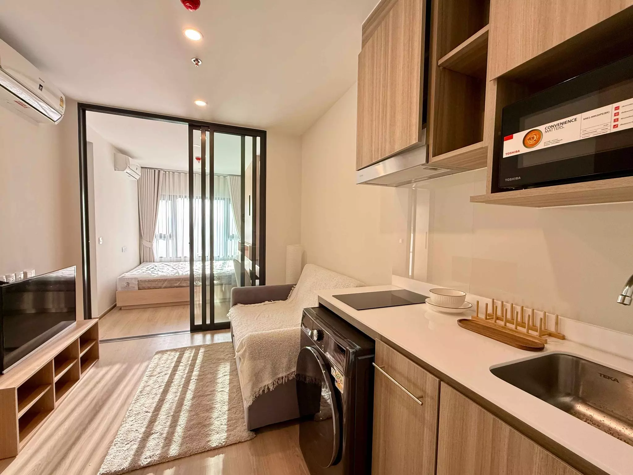 Grey sofa and wood kitchenette in compact 1-bed Life Rama 4 condo with glass bedroom divider