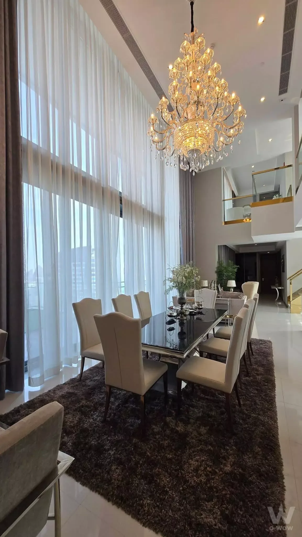 Spacious dining area in Q1 Sukhumvit Condo with crystal chandelier, glass table, and mezzanine view
