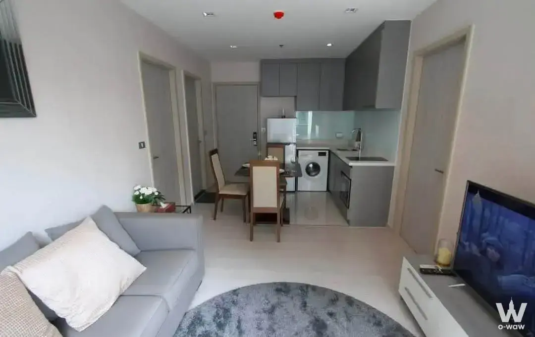 Modern open-plan living area in Rhythm Sukhumvit 2-bed condo with grey sofa and kitchen