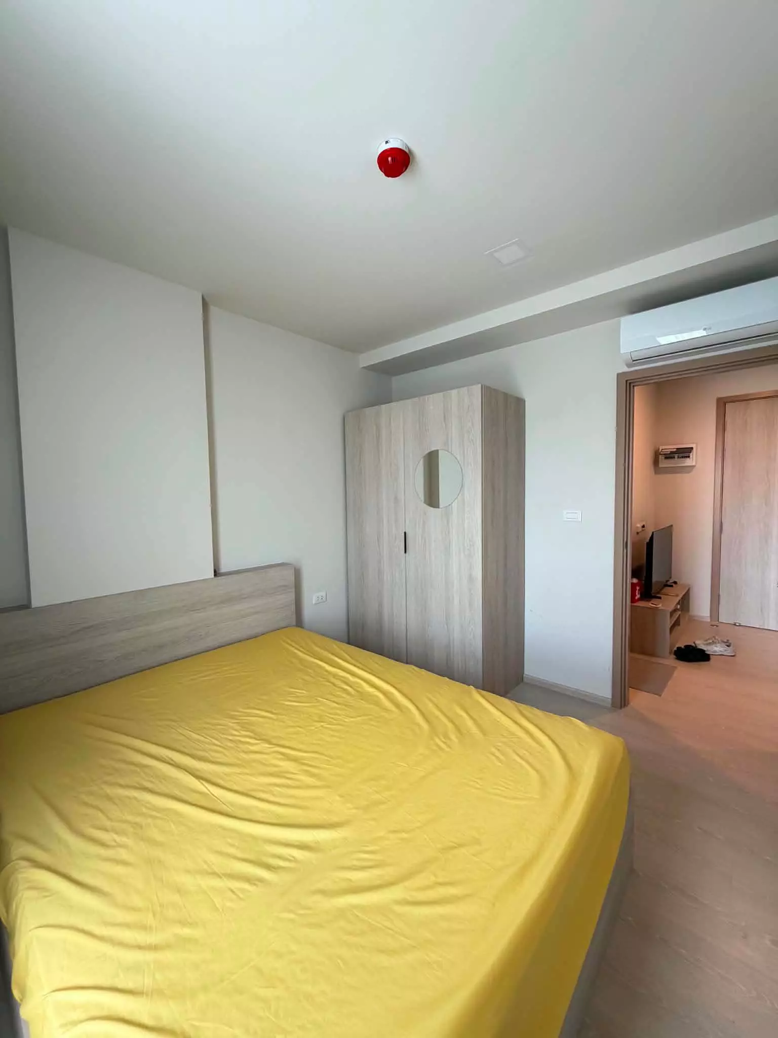 Minimalist bedroom with yellow sheets, grey headboard, and oak wardrobe in dcondo calm Ramkhamhaeng 40