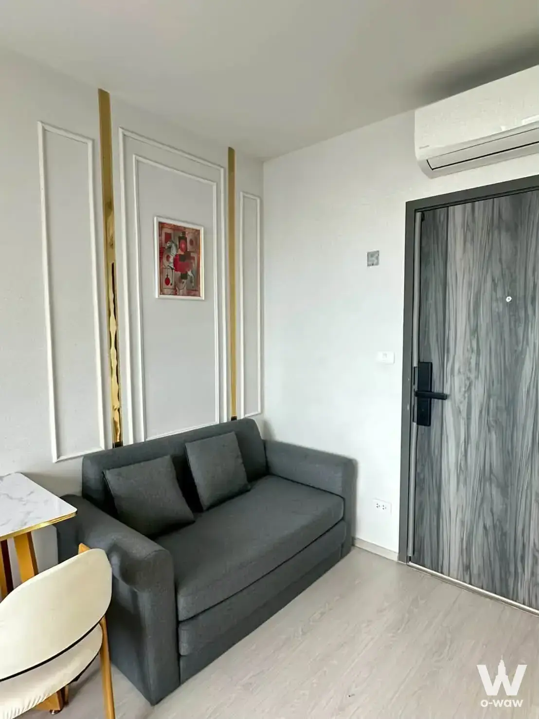 Compact living area in ELIO DEL NEST 1-bed condo featuring grey sofa, gold accents, and white feature wall paneling