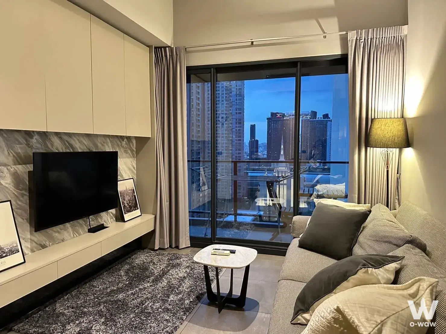 1-bed condo for sale in The Lofts Asoke living room with grey sofa and dusk skyline view