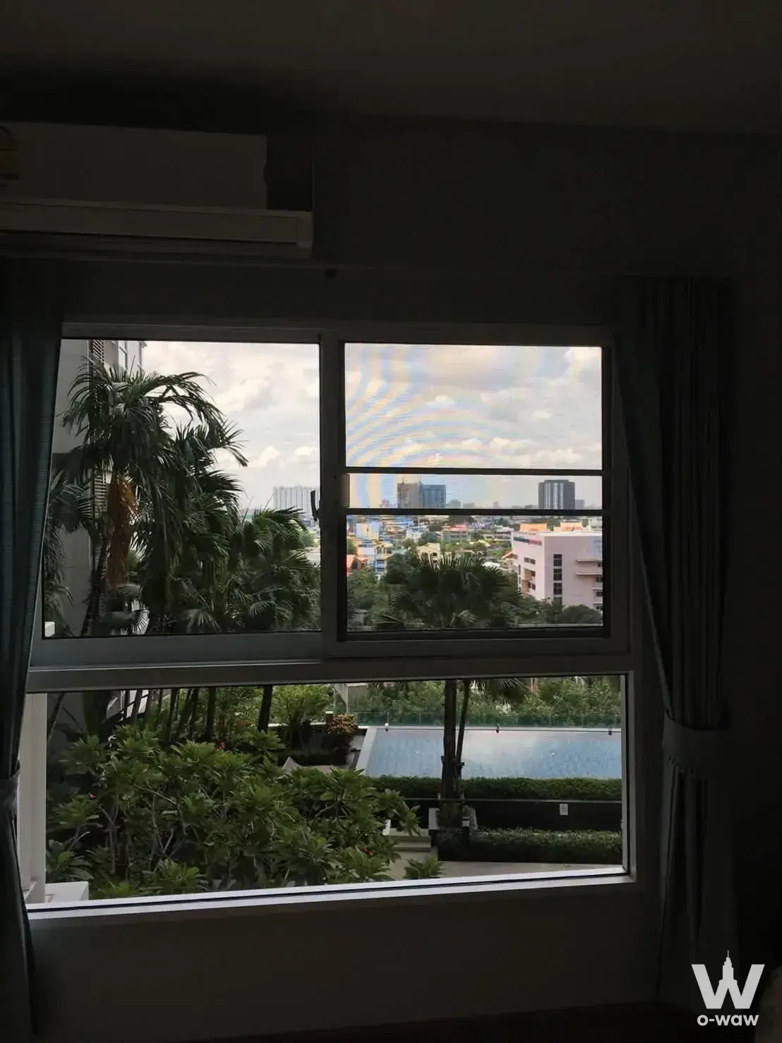 Window view of lush tropical greenery and rooftop pool from a 1-bed condo for sale at The Parkland Grand Taksin