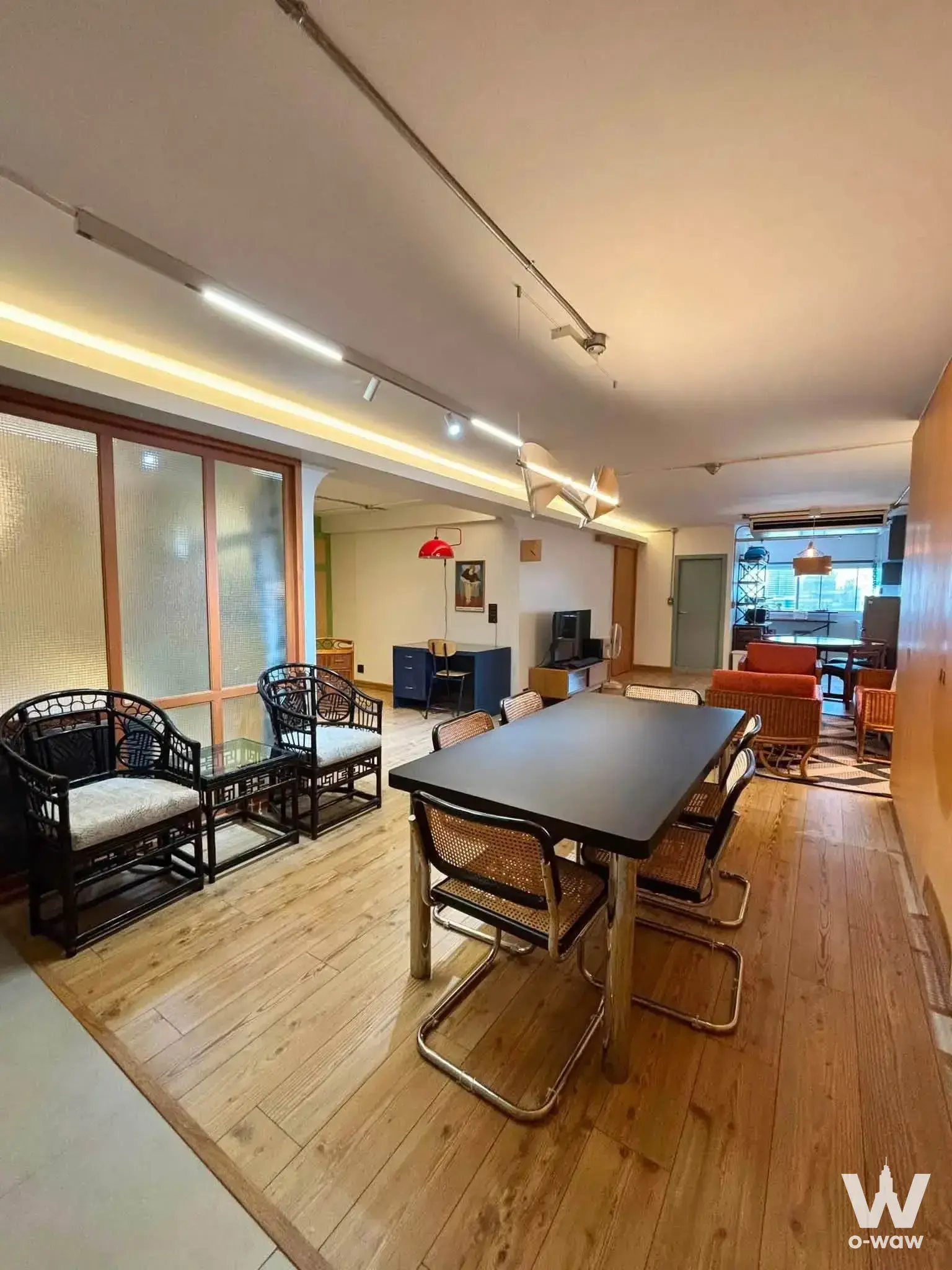 Open-plan living dining area with oak floors, black dining table, cane chairs, orange sofa, and industrial track lighting