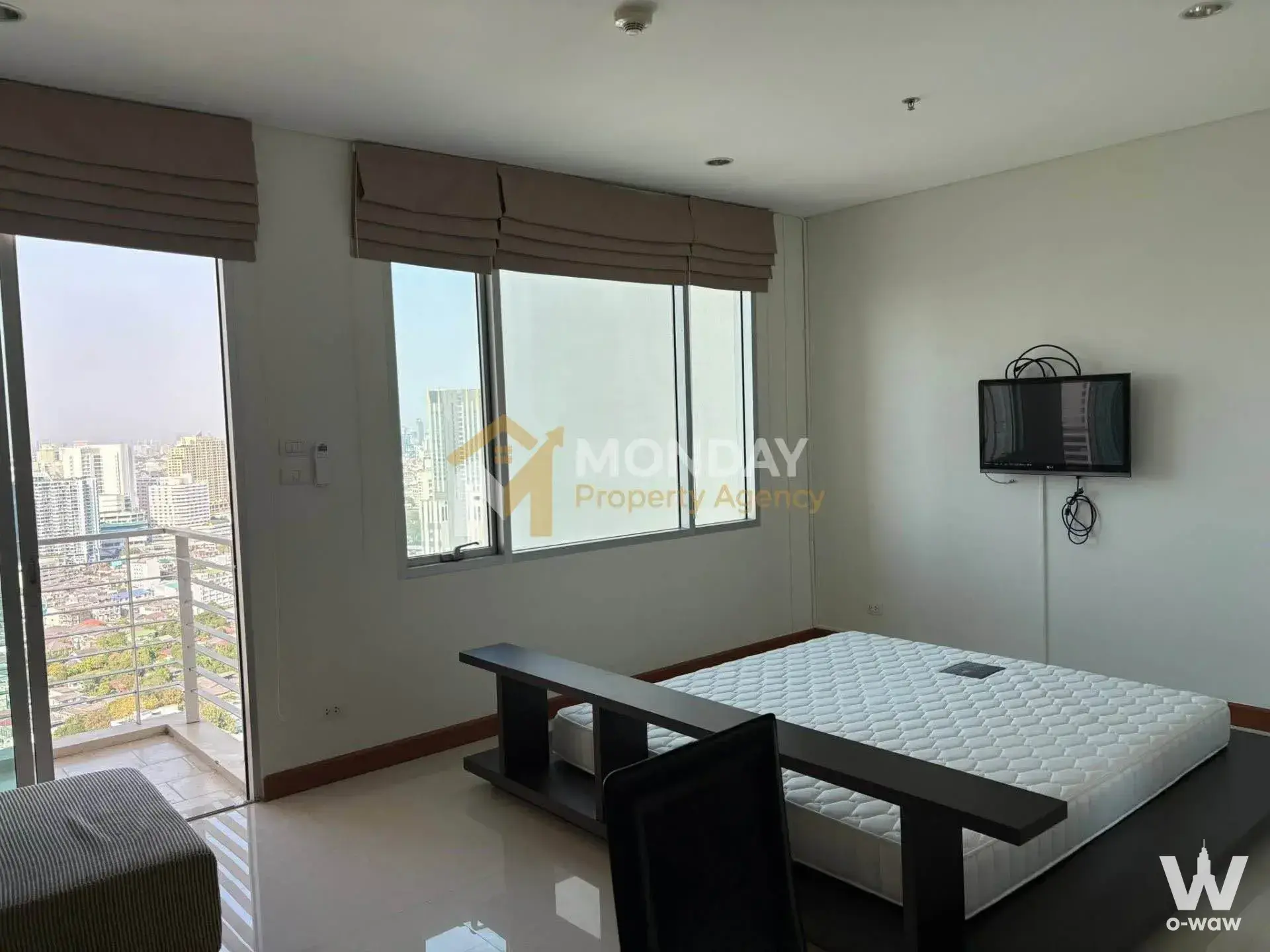 Bright bedroom in Villa Sathorn condo with dark wood bed, glossy tiles, and high-rise city views