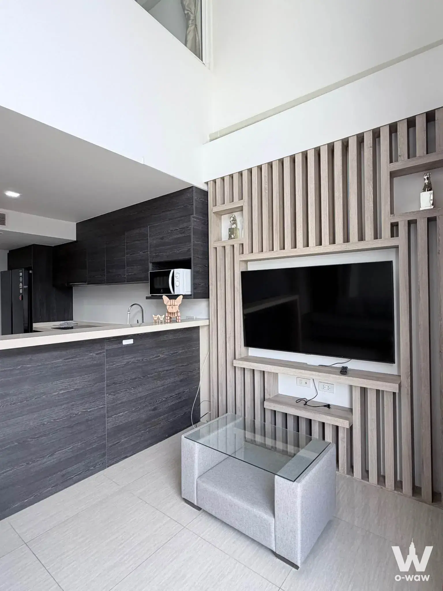 Open-plan living and kitchen in a 3-bed Downtown49 condo for rent has a wood slat TV wall, a grey armchair and a glass table