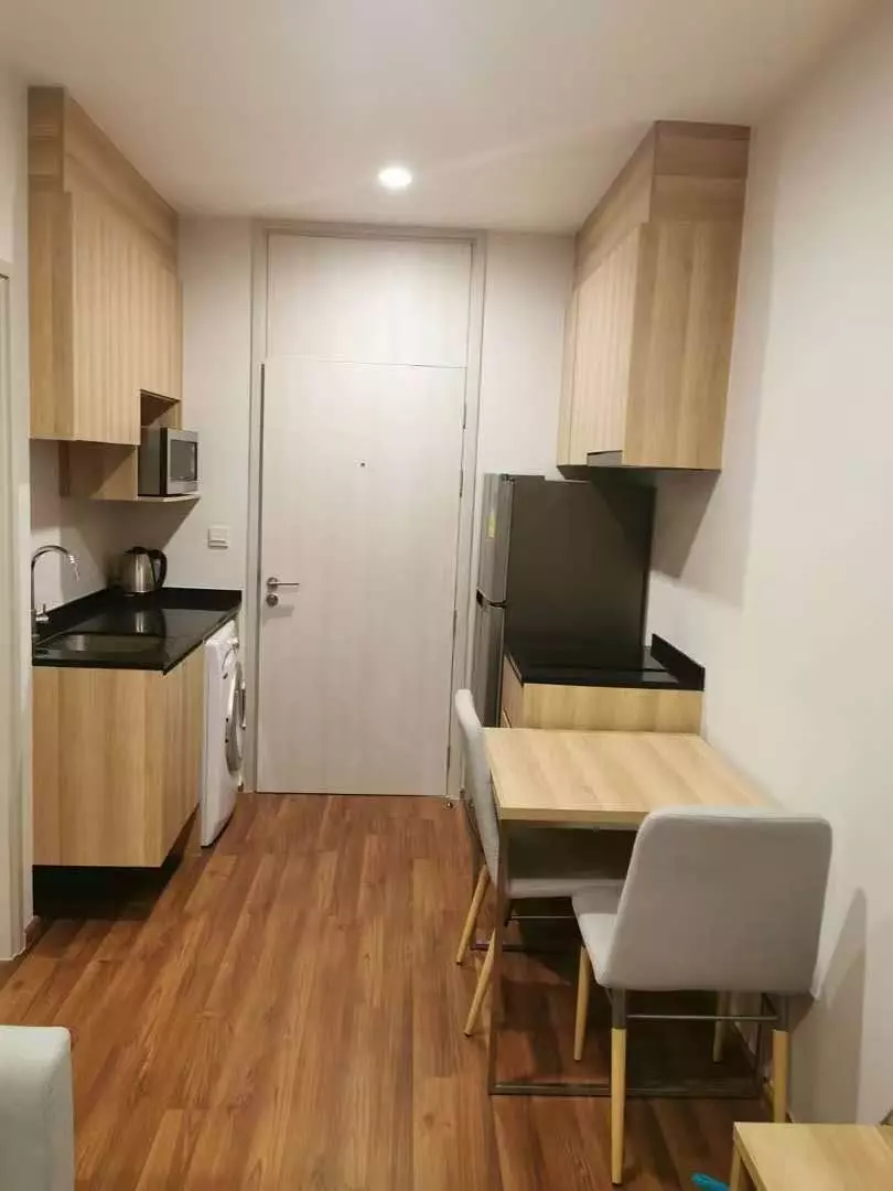 Open-plan studio kitchen and dining area with wood cabinets in Noble Revolve Ratchada 2