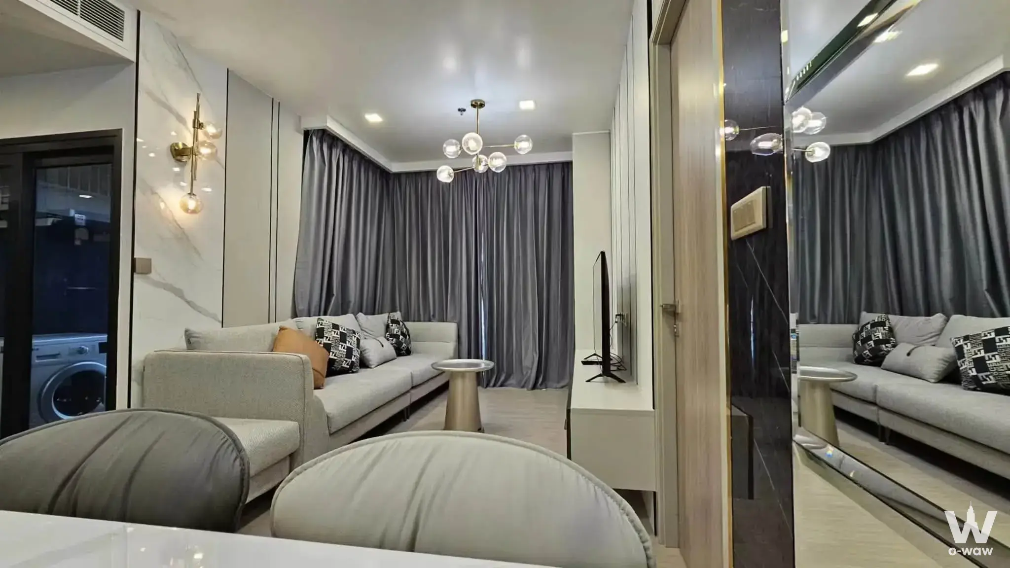 Living room of a 2-bed rental condo at One9Five Asoke featuring an L-shaped sofa and marble feature wall