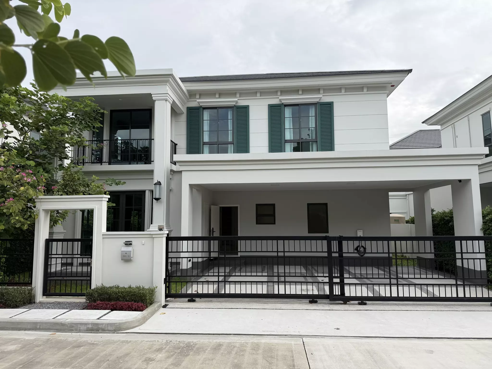 Two-story white house with green shutters and covered carport in Setthasiri Bangna