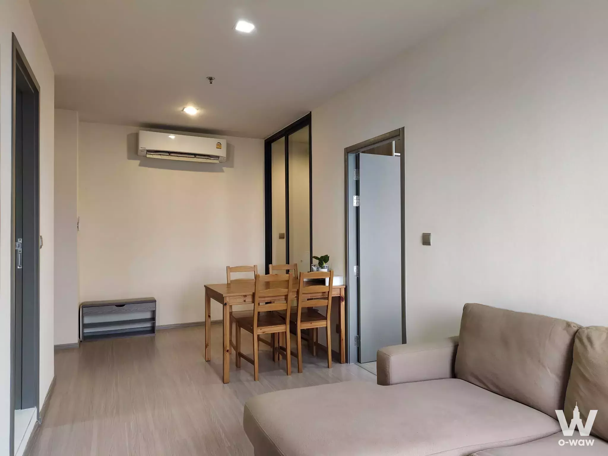 Open-plan living area in Life Asoke Hype condo featuring wooden dining set and beige sofa