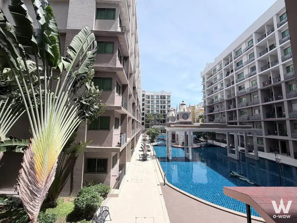 Resort-style pool area at Arcadia Beach Continental with tropical palms and a clock tower under a clear blue sky