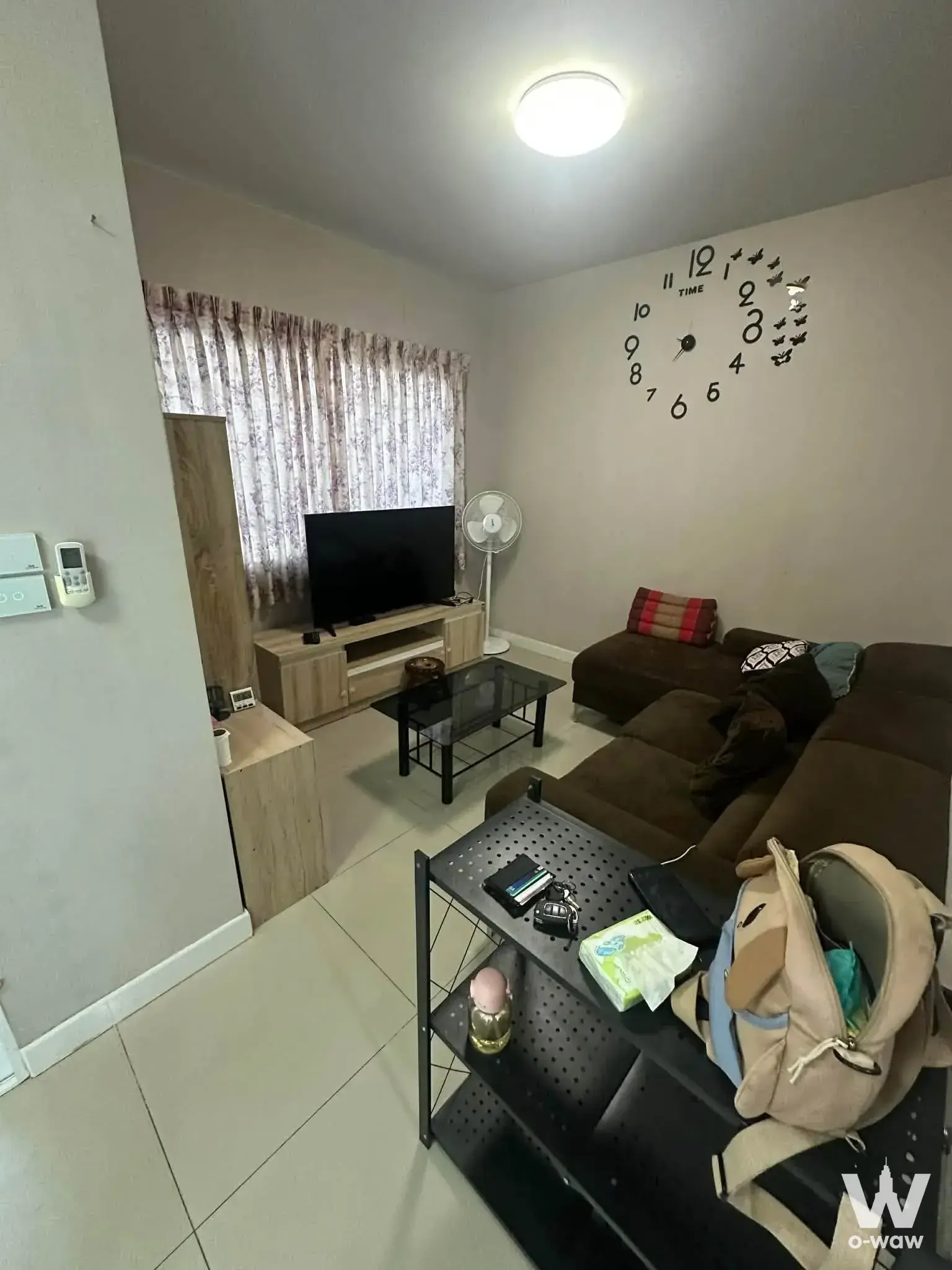 Spacious living room in The Village Bangna townhouse with brown L-shaped sectional sofa and glossy tiled flooring