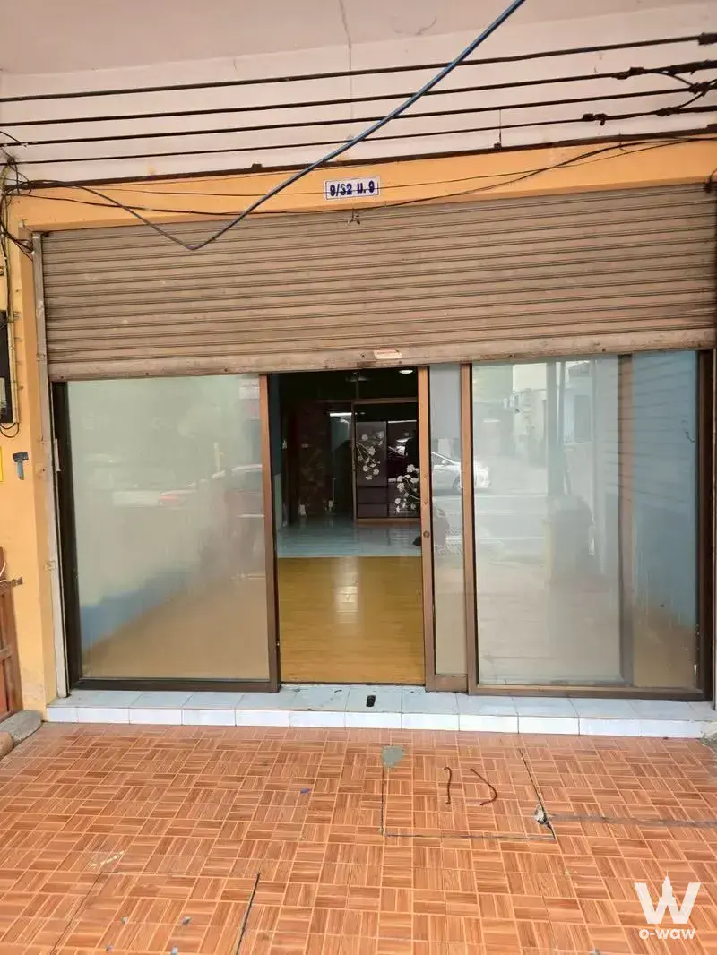 Street-level storefront facade with beige shutter, glass sliding doors, and herringbone sidewalk tiles in Siam Country Club