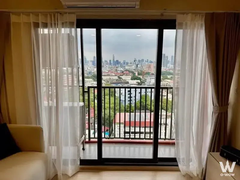 Living room in FLO by Sansiri with floor-to-ceiling glass doors opening to a balcony with city skyline view