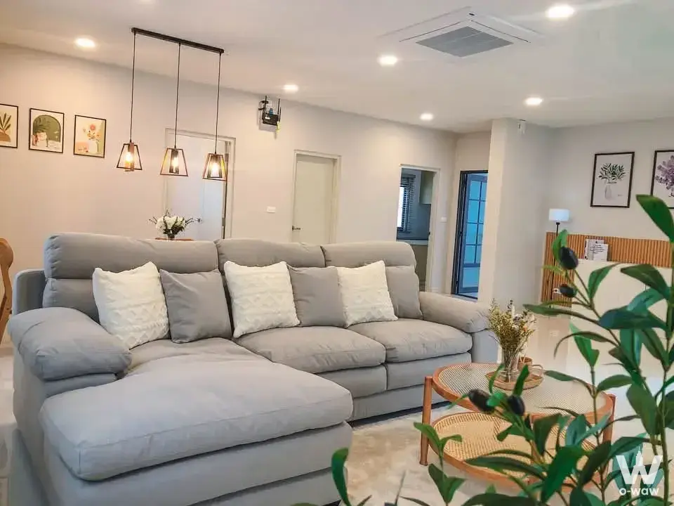 Spacious living room in Centro Bangna house with grey sectional sofa, rattan coffee table, and pendant lights