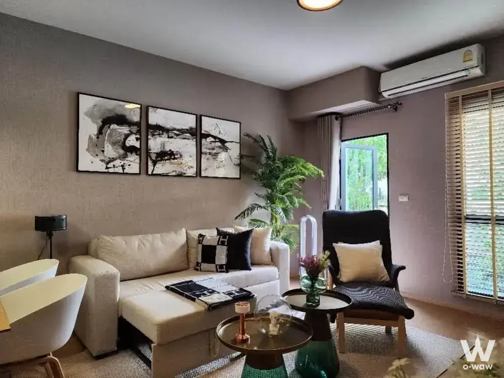 UNiO Sukhumvit 72 living room featuring taupe walls, green palm, and abstract art