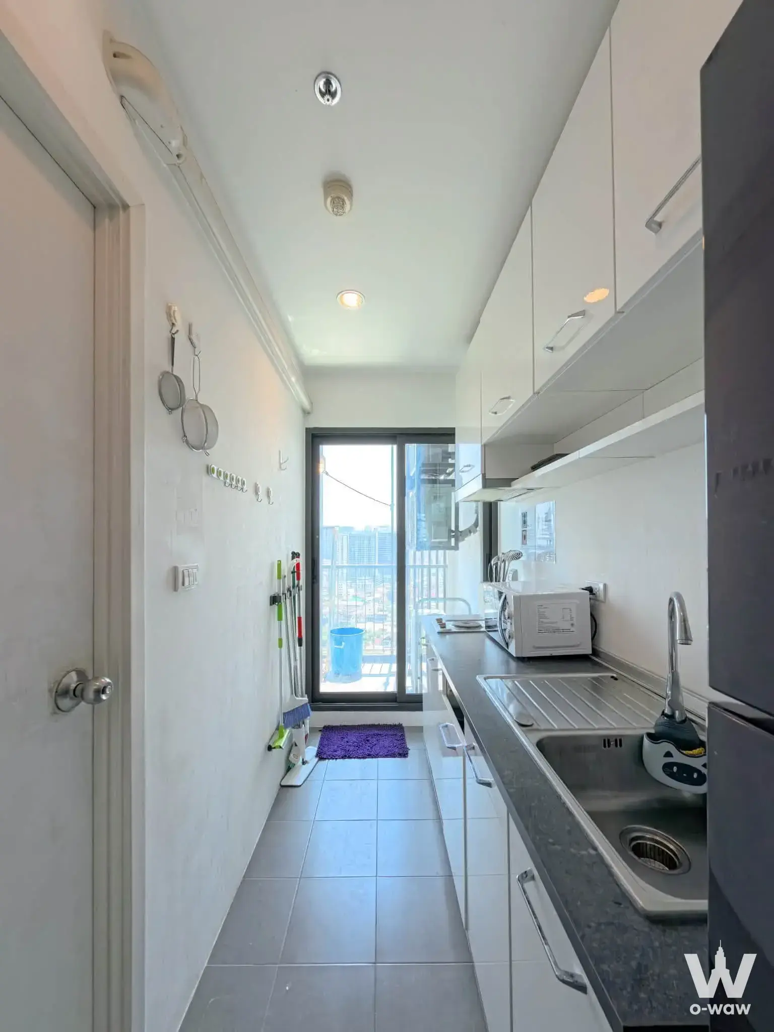 Narrow galley kitchen with white cabinets, grey tiles, and balcony access