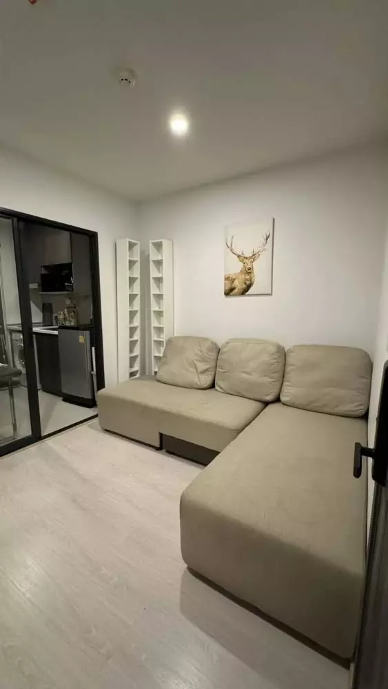 Compact living room with beige L-shaped sofa and stag art print in 1-bed condo for rent at ELIO Del Nest