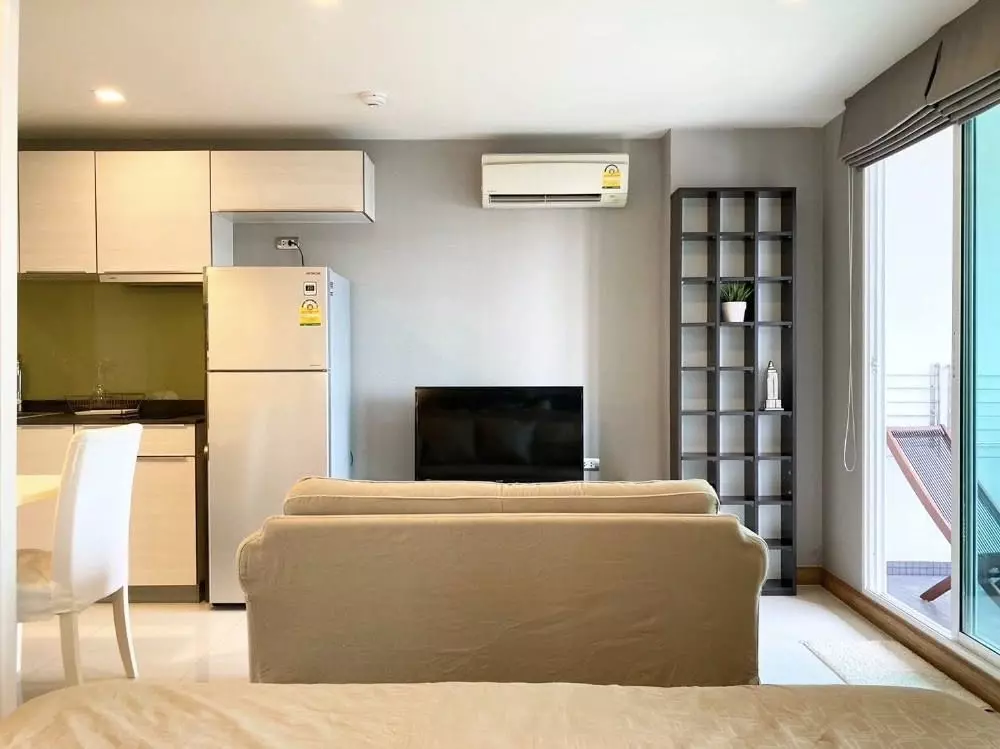 Beige sofa faces TV in Tree Condo Ekamai living area with lime-green kitchen backsplash
