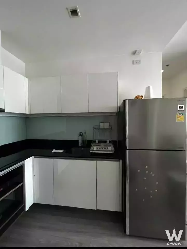 Compact modern kitchenette with white cabinets, dark countertops, and stainless steel fridge in Quinn Condo