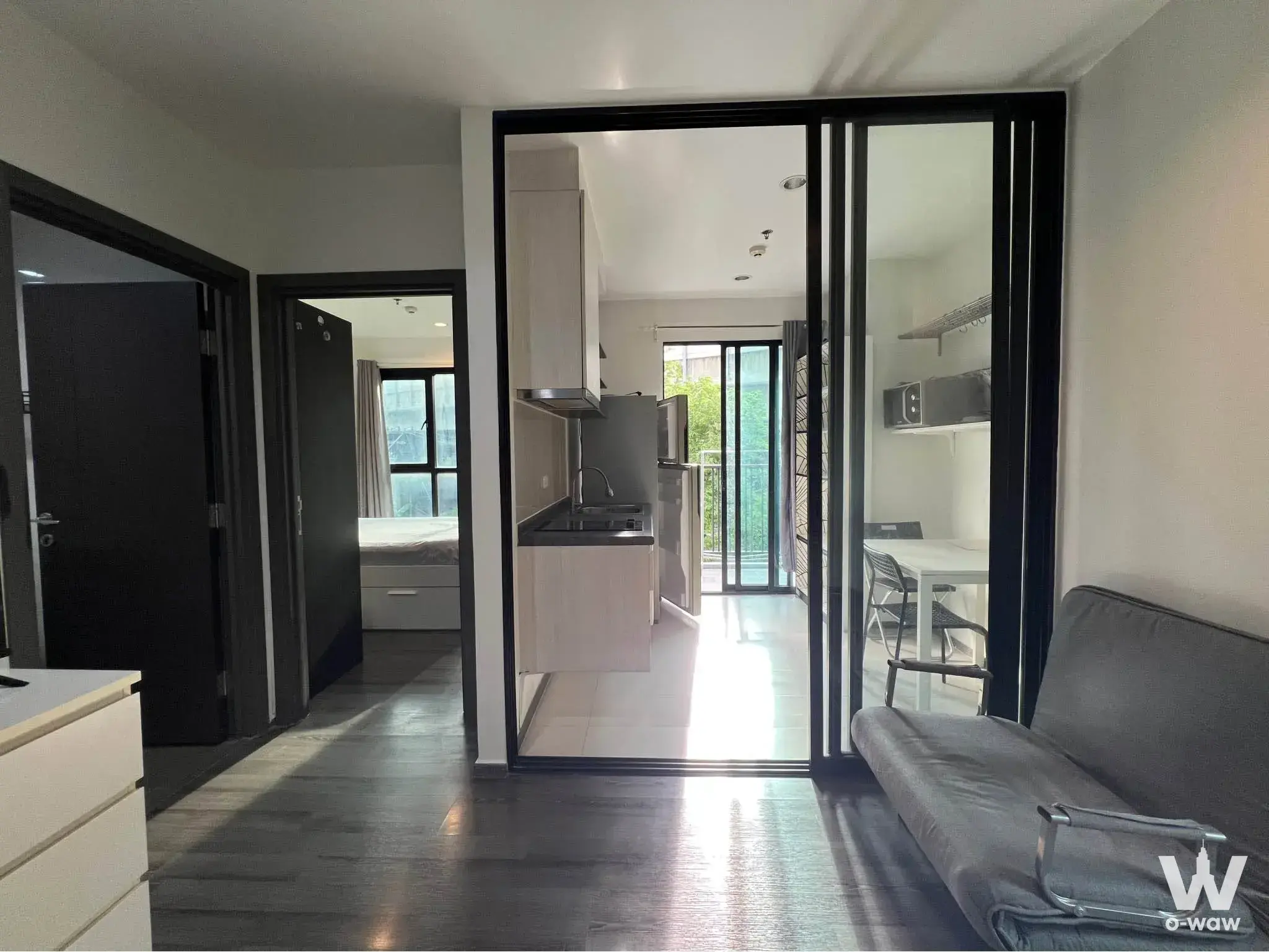 Open-plan studio in THE BASE Park West Sukhumvit 77 rental showing grey sofa bed and kitchen with black bi-fold doors
