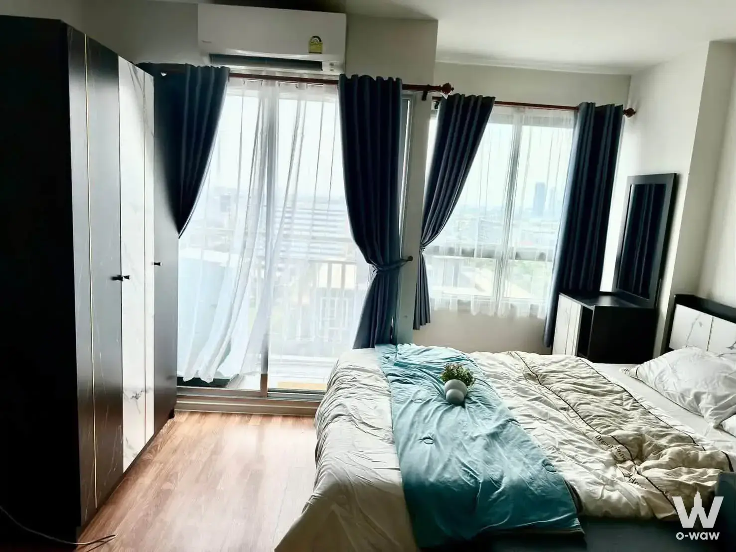 Bedroom in Lumpini Ville Pattanakarn condo with teal accents, balcony doors, and city view