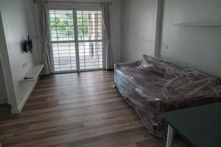 Living room in 3-bed condo at The Metro Sathorn with wood floors, plastic-covered sofa, and balcony doors
