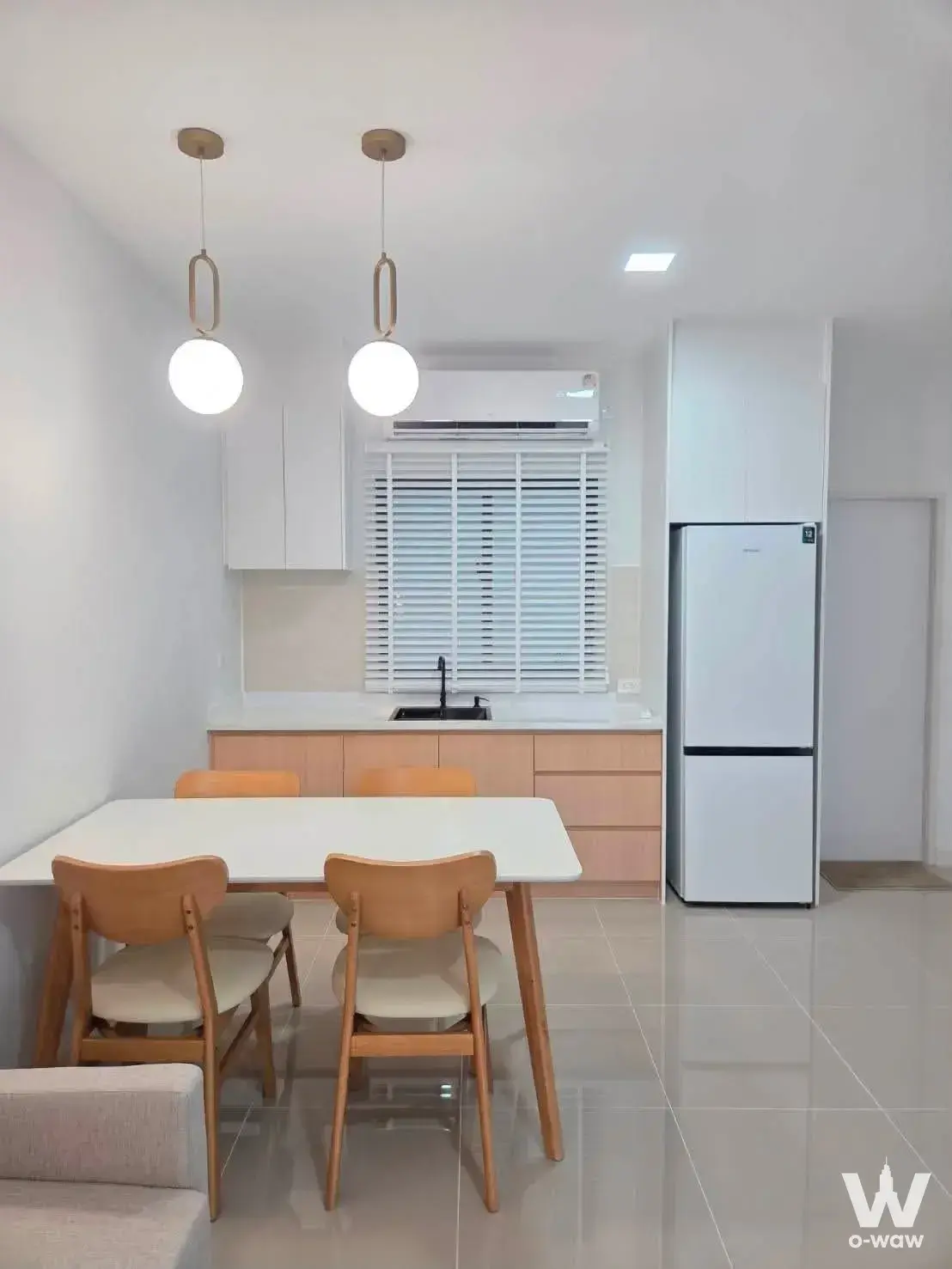 Open-plan dining area in Pleno Sukhumvit-Bangna house featuring white table, oak chairs, gold pendants, and compact