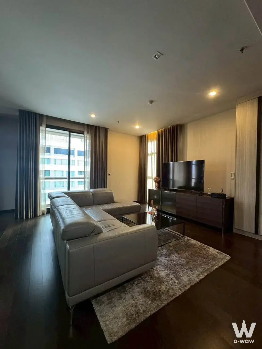 Modern living room in a 2-bed condo at THE XXXIX by Sansiri featuring a grey leather sectional and dark wood floors