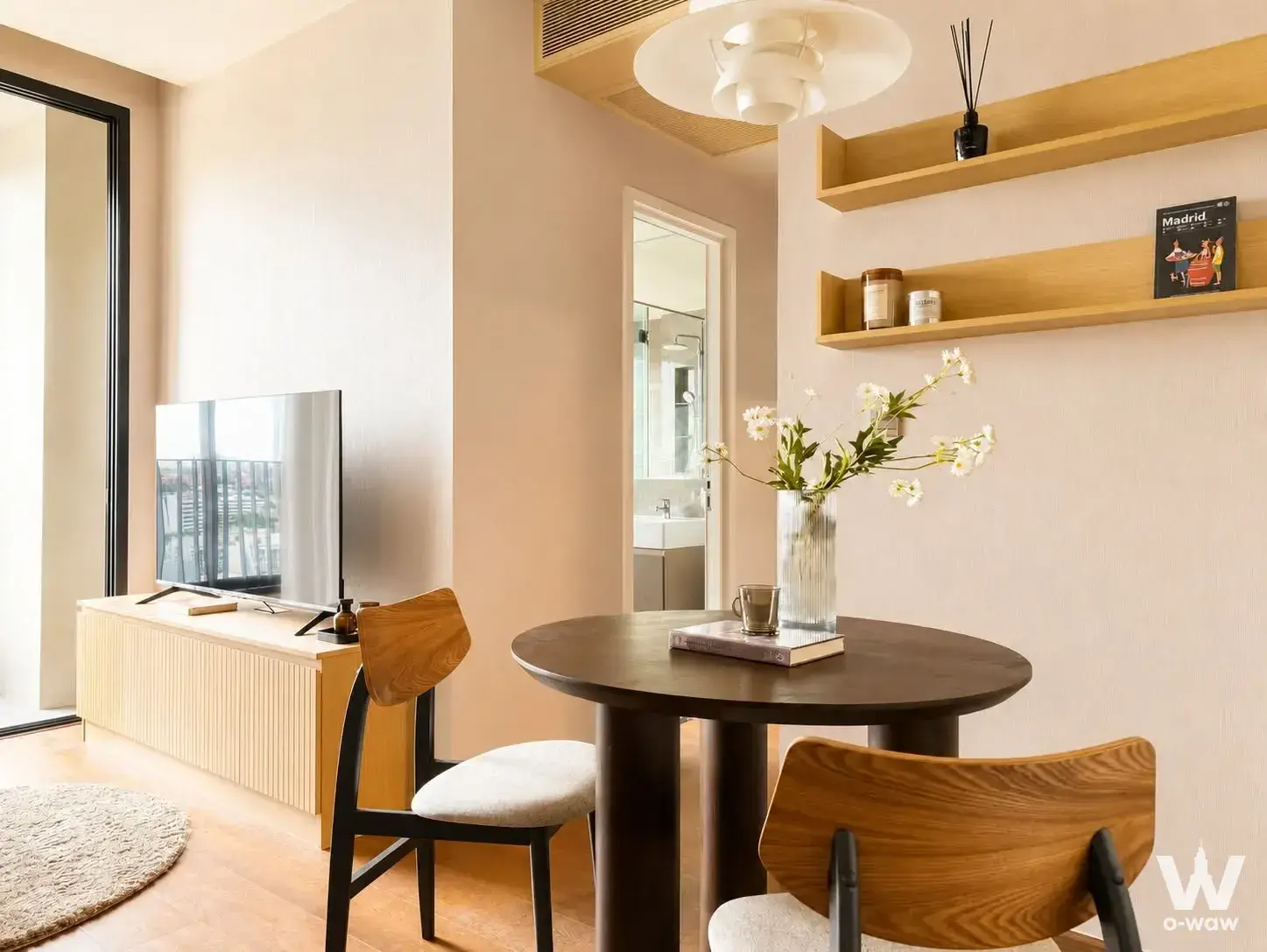 Open-plan living area with round wooden dining table, TV console, and sliding glass door to balcony
