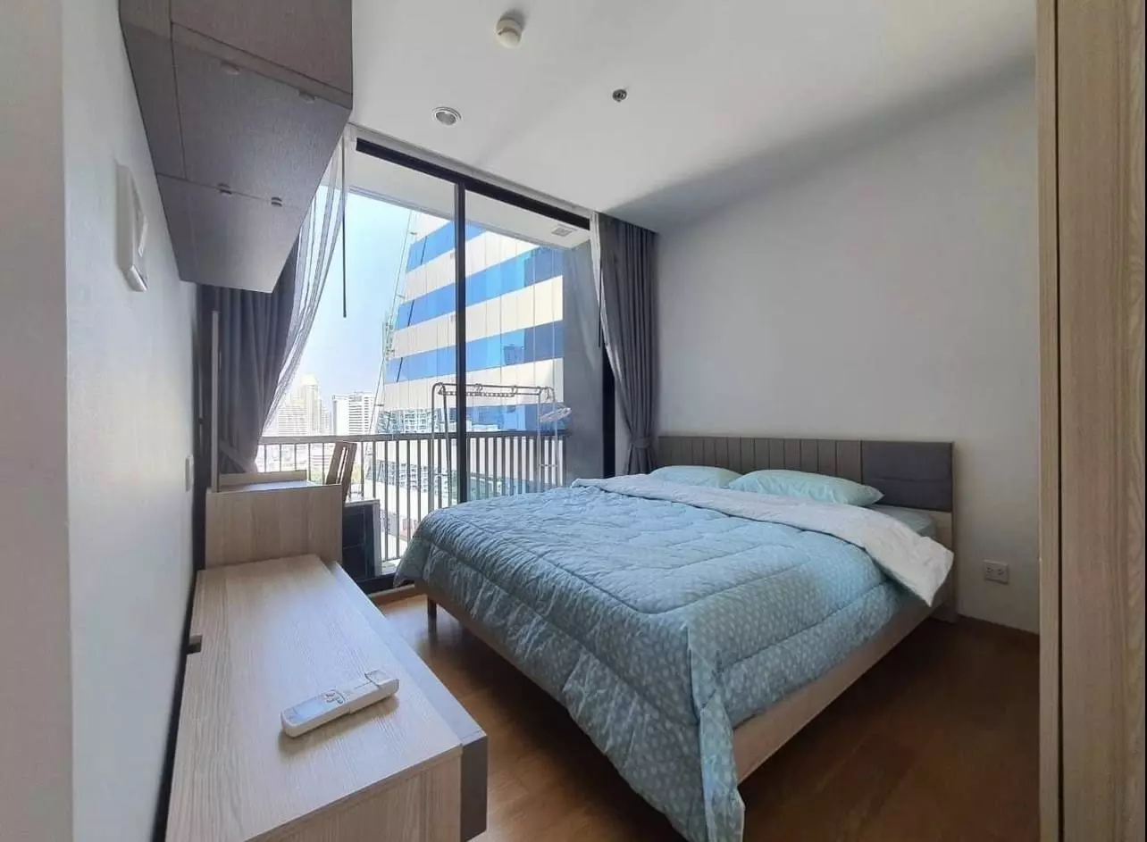 Bedroom with grey headboard and built-in desk in 1-bed Noble Revo Silom condo for rent