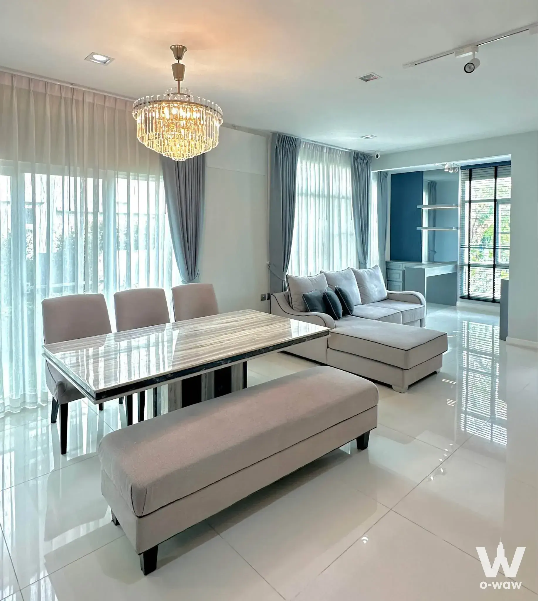 Bright open-plan living and dining area with crystal chandelier, marble table, and floor-to-ceiling windows in this 4-bed