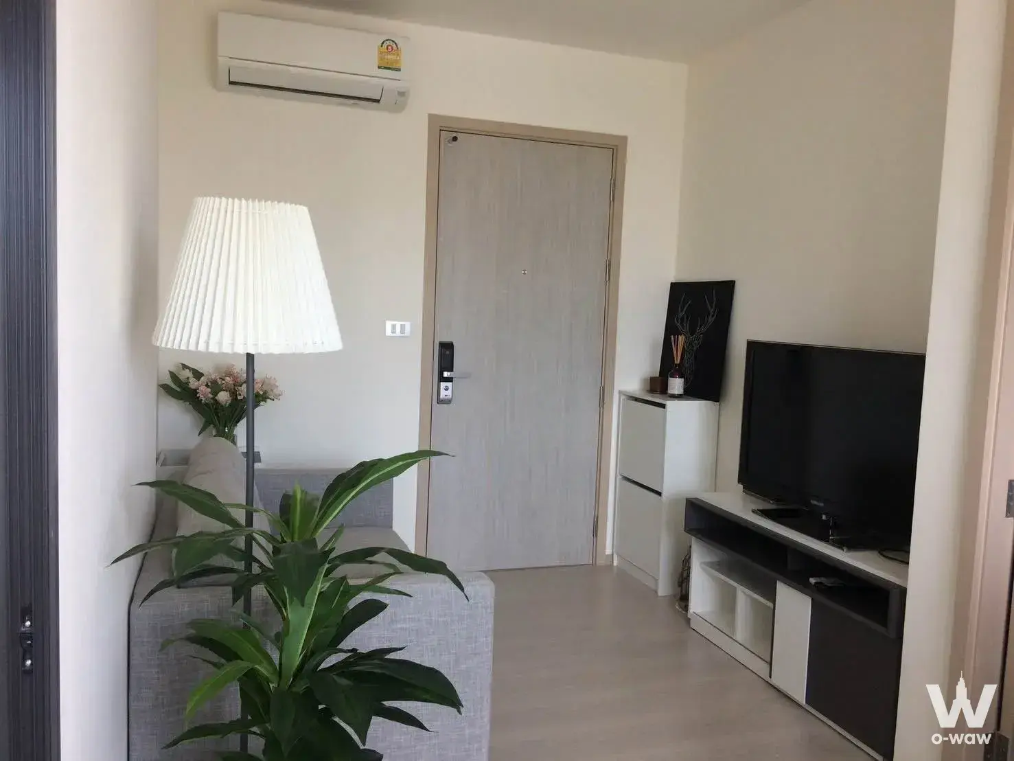 Compact modern living room in Rhythm Sukhumvit 36-38 condo with grey sofa, smart lock entry door, and media console