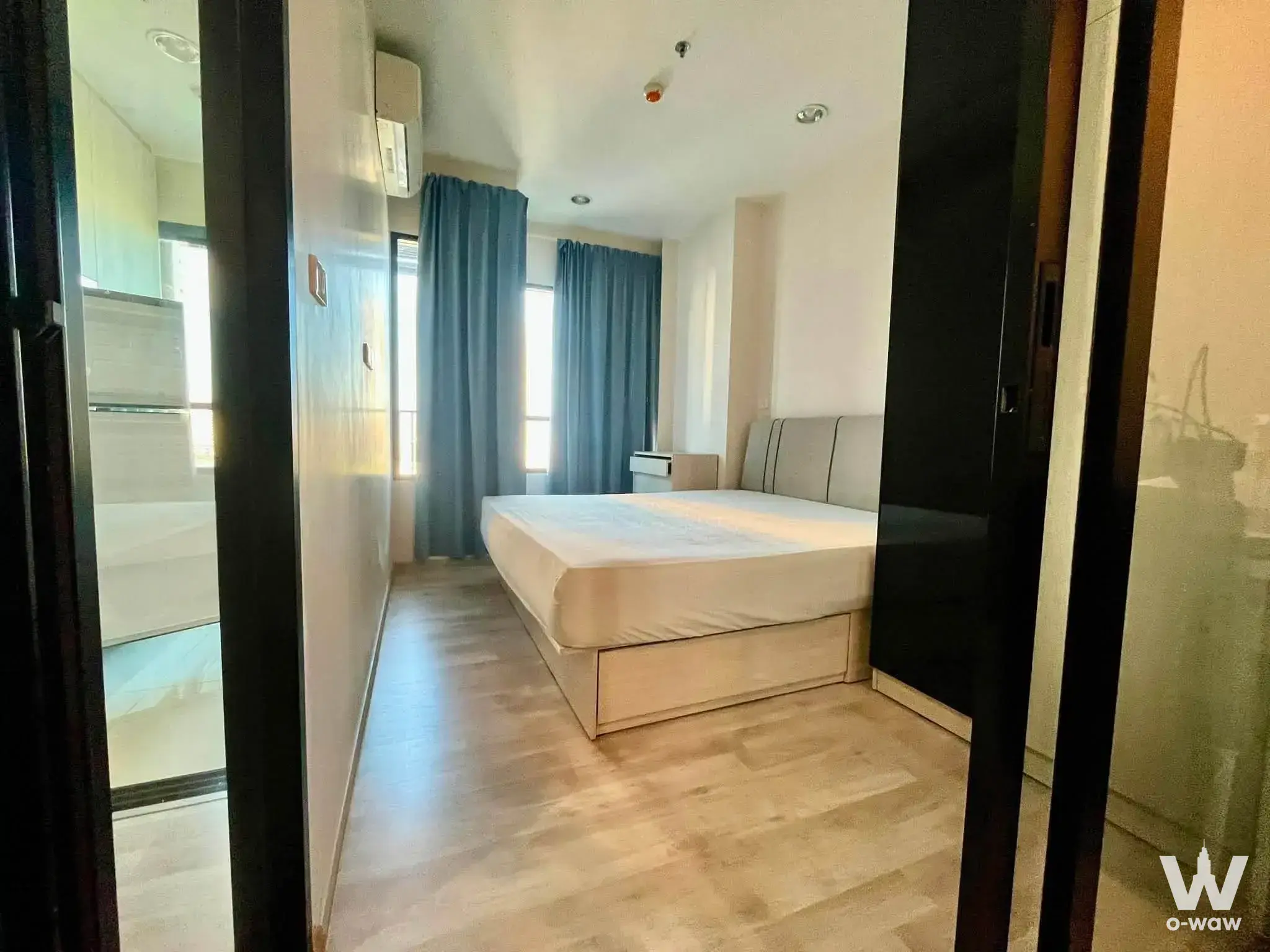 Minimalist bedroom with beige bed, teal curtains, and light wood flooring