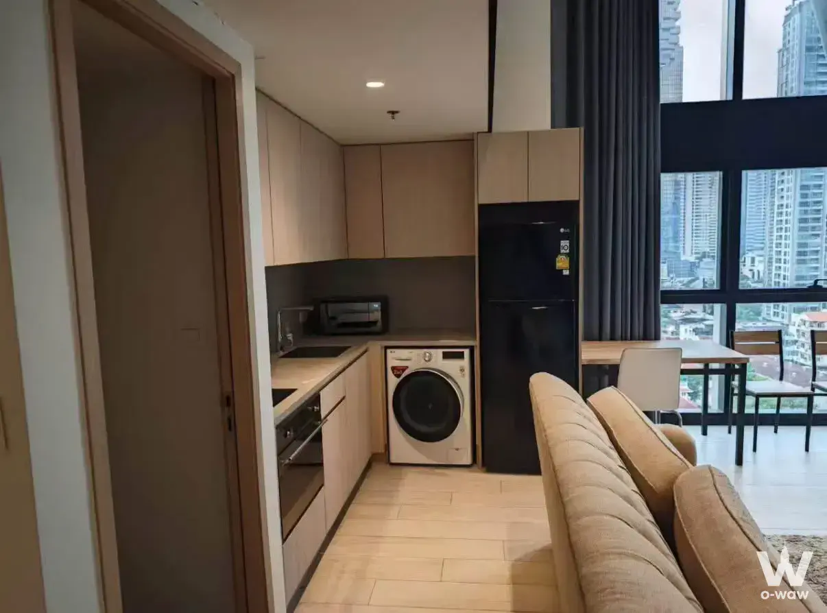 Open-plan studio with light wood laminate floor, compact kitchen, and high-rise city view in The Lofts Silom