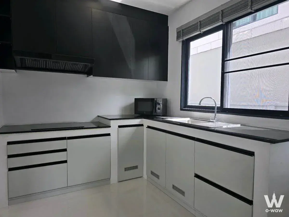 Sleek L-shaped kitchenette with glossy white cabinets, black countertops, and double sink in Centro Vibhavadi