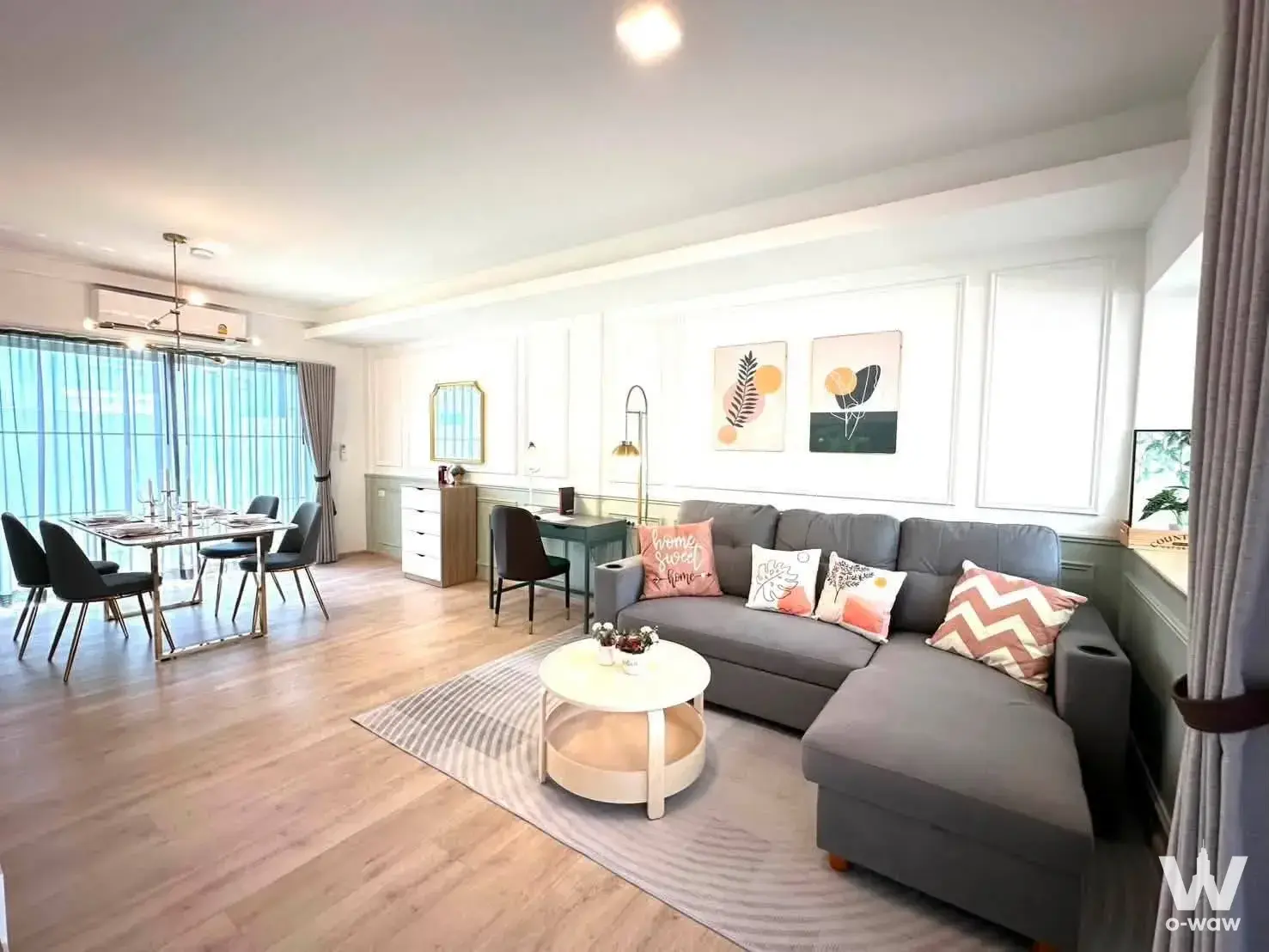 Spacious living and dining area featuring a grey sectional sofa, botanical art, and sage green wall paneling in this fully