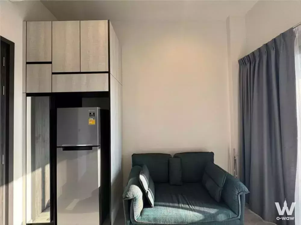 Minimalist living area with teal sofa, light wood cabinet housing fridge, and floor-to-ceiling grey curtains