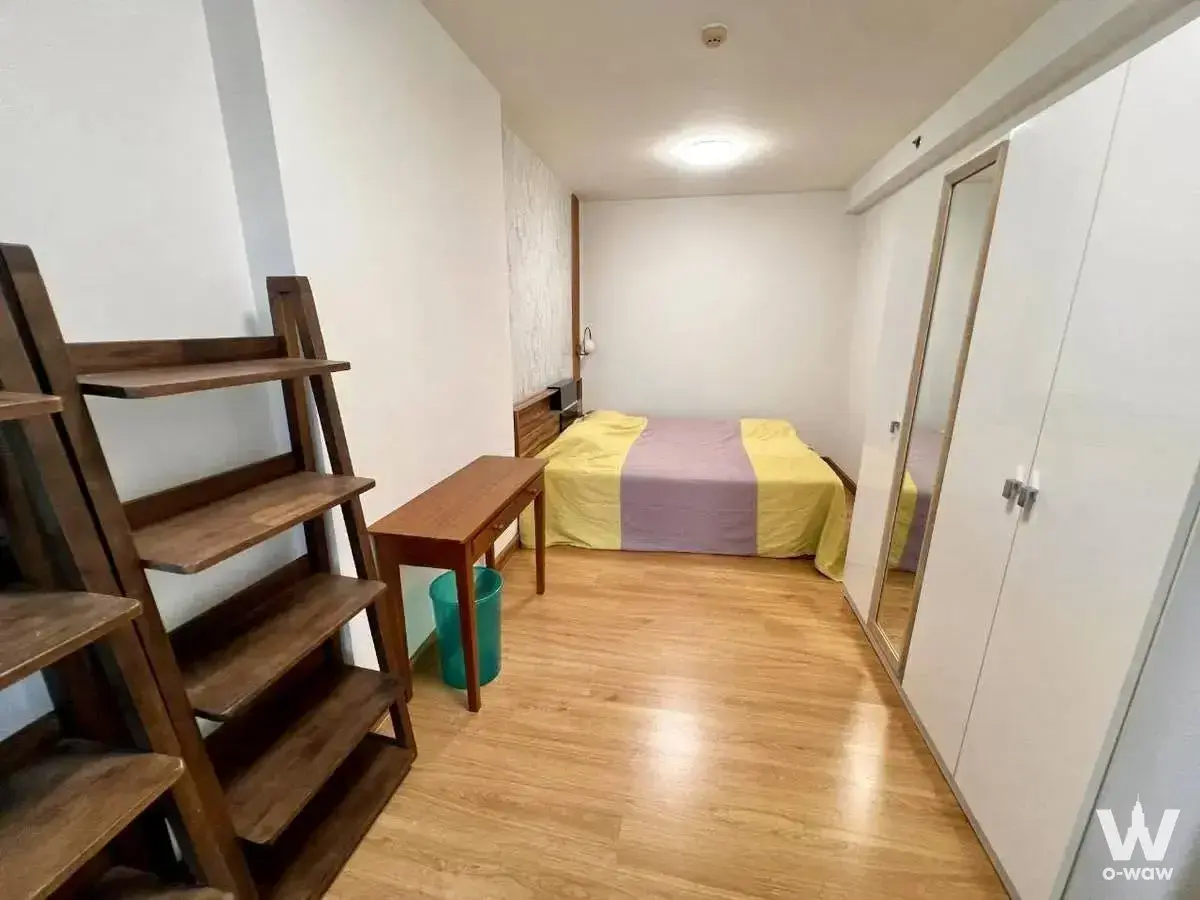 Compact bedroom in a Supalai Park 1-bed condo featuring dark wood shelving and colorful striped bedding